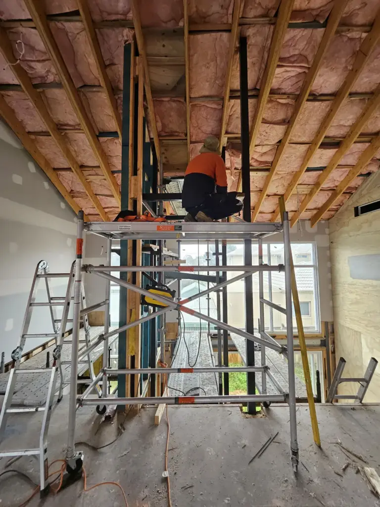 Steel lift shaft structure being installed through the ceiling of an existing home, with mobile scaffold and installer at height