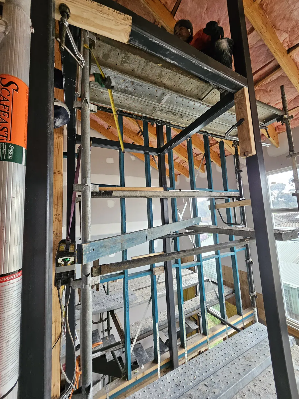 Lift shaft steel frame being checked for vertical alignment inside existing timber framing